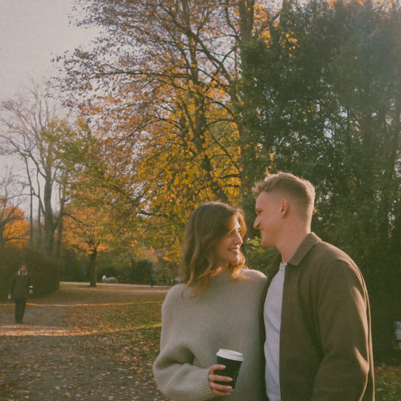 Elise en Thomas wandelen met koffie tussen dwarrelende herfstbladeren op hun eerste date