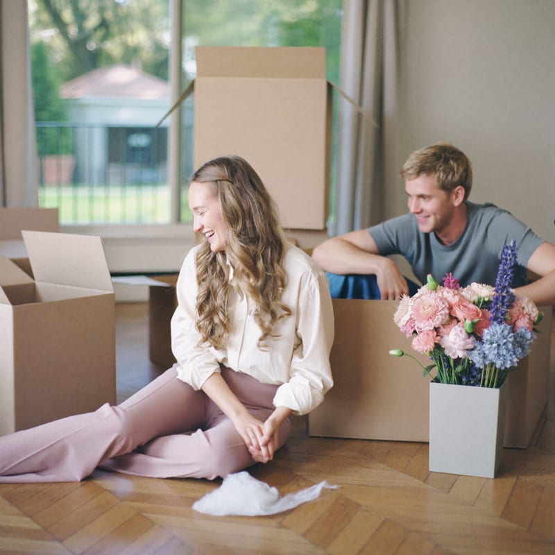 Elise en Thomas lachend tussen de verhuisdozen op de vloer van hun eerste huisje